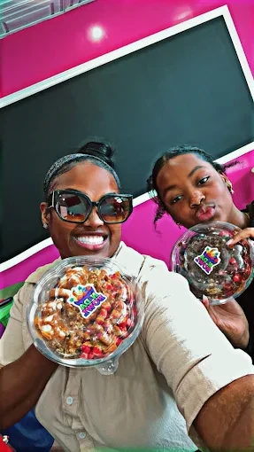 Two smiling customers holding N Da Bowl bowls inside the pink shop